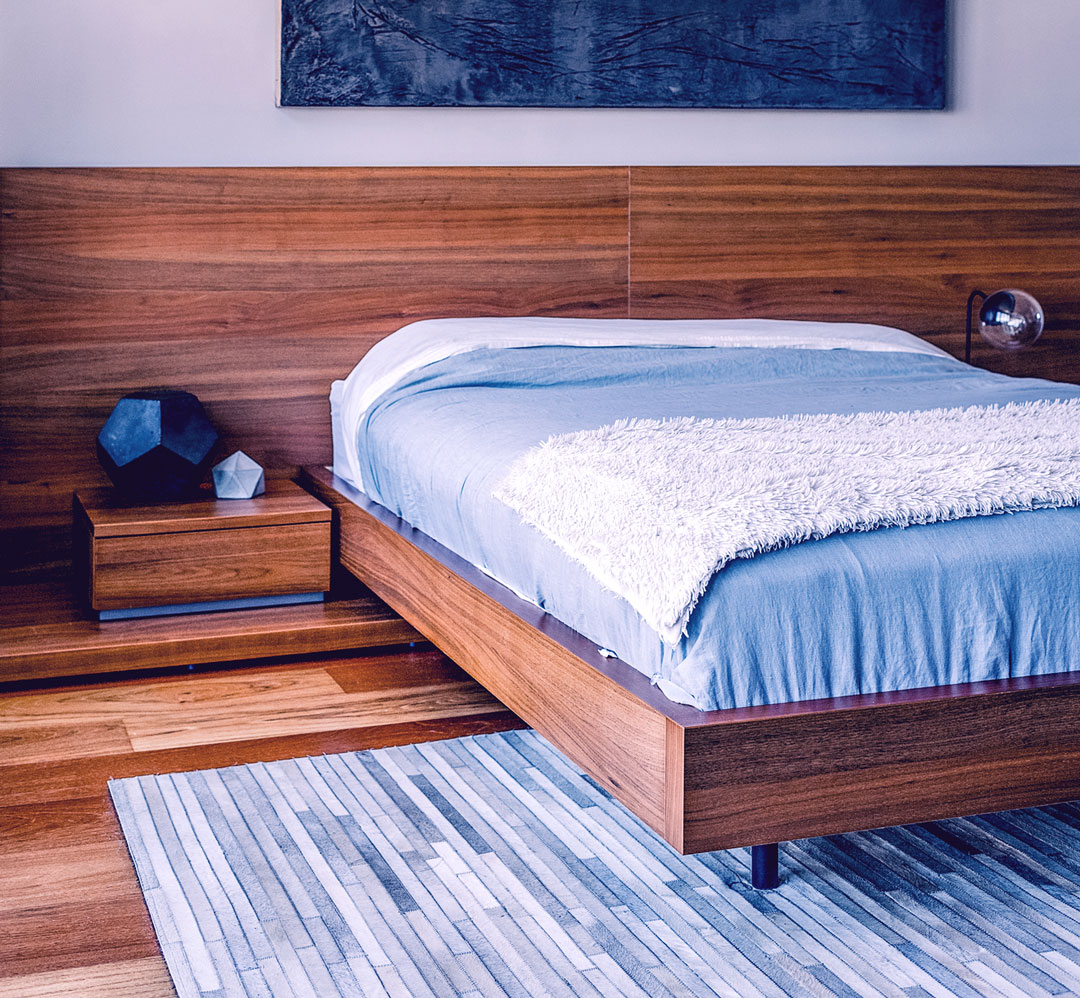 Wooden platform bed with blue bedding and a white fluffy throw in a modern bedroom   Nerds On Site