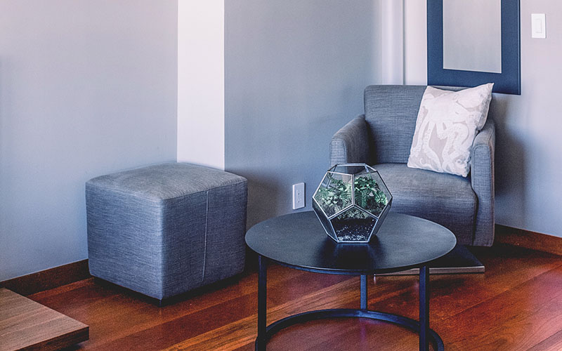 Gray armchair with a matching ottoman and a round black coffee table featuring a geometric glass terrarium centerpiece in a cozy living room corner   Nerds On Site